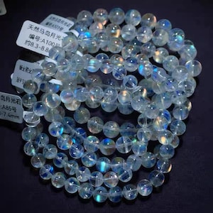 Op de afbeelding: Verschillende strengen heldere, iriserende maansteen kralenarmbanden. De kralen zijn rond en hebben een subtiele blauwe en regenboogglans. De afbeelding bevat kleine witte labels met Chinese tekst en afmetingen in millimeters.
