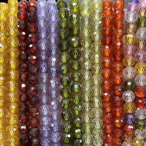 May include: Multiple strands of faceted round beads arranged in a vertical display. The beads feature a variety of translucent colors including purple, yellow, red, light purple, green, lime, orange, pink, and clear, each with a reflective surface.