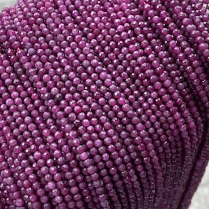 May include: A strand of deep purple faceted gemstone beads. The beads are round and have a smooth, polished finish.