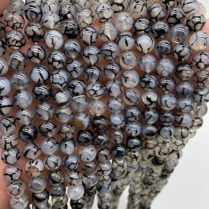 May include: A strand of round, white agate beads with black dendritic patterns. The beads are smooth and polished.