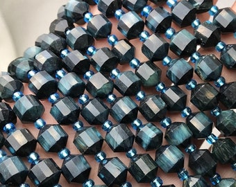 May include: Close-up of multiple strands of faceted, dark teal gemstone beads. Each bead is a geometric shape with a dark teal color and is separated by small, light blue beads. The beads are strung together, creating a textured surface.