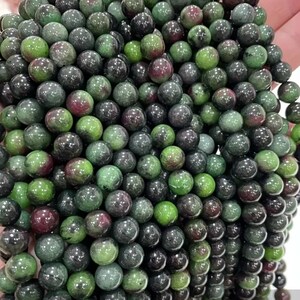 May include: A strand of green and black gemstone beads. The beads are round and have a smooth, polished finish.