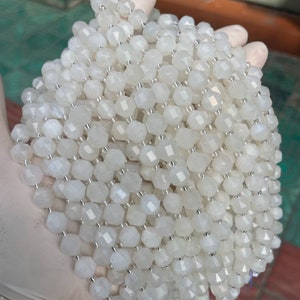 May include: A strand of white moonstone beads, each bead is faceted and has a hexagonal shape.