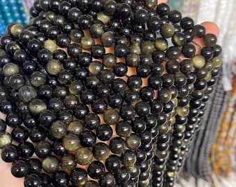 May include: A strand of black and gold gemstone beads. The beads are round and have a smooth, polished finish. The beads are strung on a clear elastic cord.