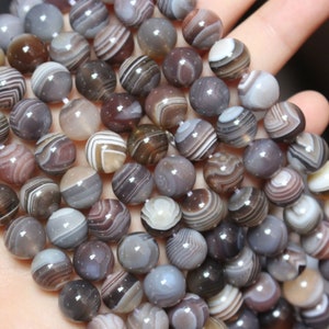May include: A strand of agate beads with brown, white and grey stripes. The beads are round and have a smooth, polished finish.