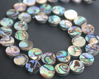 Peut inclure: Un brin de perles d'ormeau irisées. Les perles sont rondes et plates, avec une variété de couleurs et de motifs. Les perles sont enfilées sur un fil transparent.