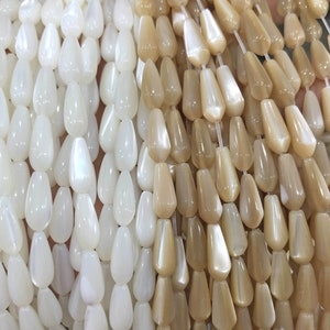 May include: A strand of white and beige teardrop-shaped beads made of mother of pearl. The beads are strung on clear elastic thread.