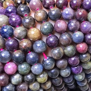 May include: A strand of round, multi-colored gemstone beads. The beads are a mix of blue, green, purple, and brown.