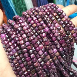May include: Strands of faceted, deep red ruby beads. The beads are small, square-cut, and strung together, creating a rich, textured appearance. The color varies from light to dark red, with some beads appearing almost purple.