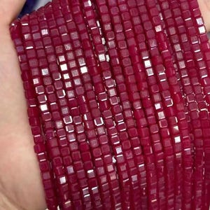 May include: A strand of red square-shaped beads with a shiny, faceted finish.