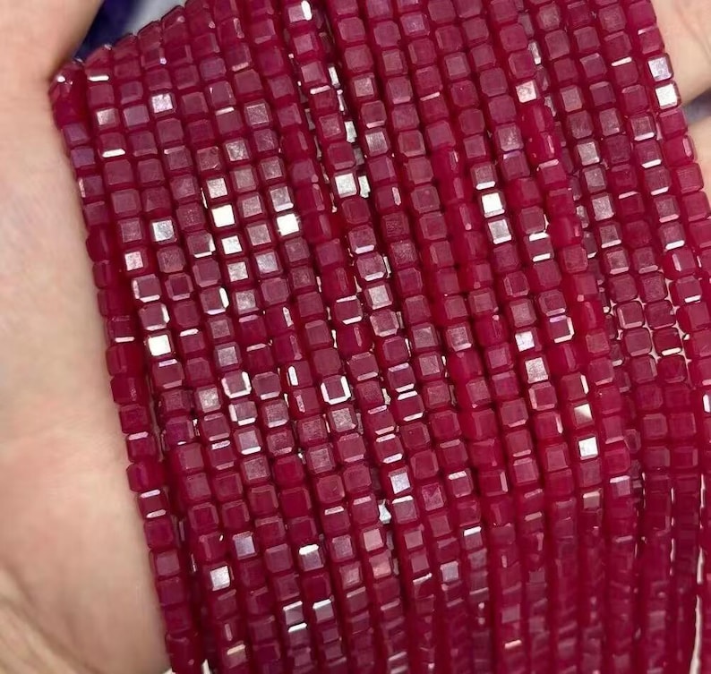 May include: A strand of red square-shaped beads with a shiny, faceted finish.