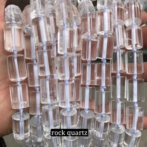 May include: A strand of clear rock quartz beads, each bead is a faceted cylinder with a smooth, polished finish. The beads are strung on a white thread and are arranged in a straight line. The text "rock quartz" is visible at the bottom of the image.