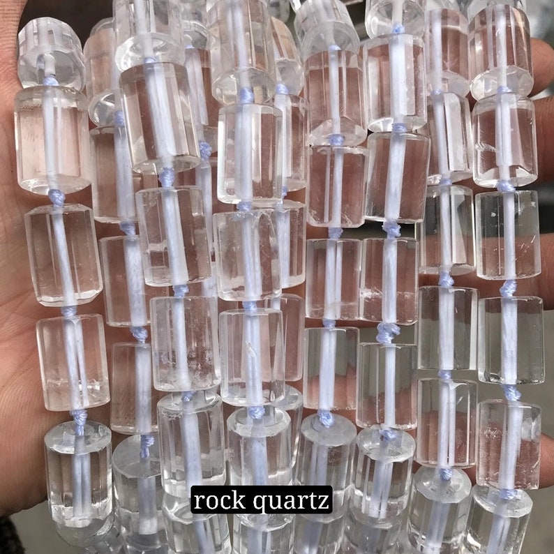 May include: A strand of clear rock quartz beads, each bead is a faceted cylinder with a smooth, polished finish. The beads are strung on a white thread and are arranged in a straight line. The text "rock quartz" is visible at the bottom of the image.