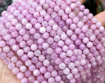 Puede incluir: Una hebra de cuentas de piedras preciosas de color rosa pálido y lavanda. Las cuentas son redondas y lisas, con una apariencia ligeramente translúcida.