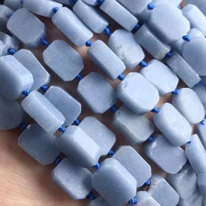May include: A strand of light blue gemstone beads, each bead is faceted and has a rectangular shape. The beads are strung on blue thread.