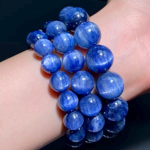 Könnte beinhalten: Ein Armband mit großen, runden, polierten Perlen in einem tiefen, satten Blau. Die Perlen haben ein subtiles, wirbelndes Muster und sind zu einem tragbaren Accessoire aufgereiht. Das Armband wird am Handgelenk gezeigt.