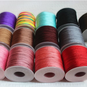 May include: Assortment of spools of colorful waxed cotton cord, each wound around a clear plastic bobbin. The colors include turquoise, brown, red, pink, gray, black, brown, green, and purple.