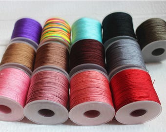May include: Assortment of spools of colorful waxed cotton cord, each wound around a clear plastic bobbin. The colors include turquoise, brown, red, pink, gray, black, brown, green, and purple.
