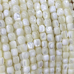 Può includere: Una collana di perline quadrate bianche in madreperla. Le perline hanno una leggera lucentezza iridescente.