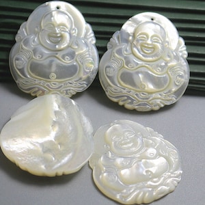 May include: Four carved mother-of-pearl pendants. Two pendants depict a smiling Buddha figure with intricate details. The other two are a shell and a Buddha pendant. The pendants are white with a pearlescent sheen.