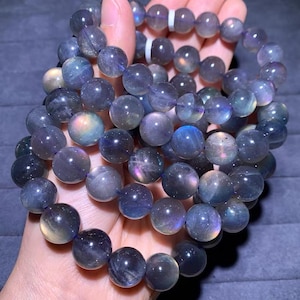 Puede incluir: Primer plano de dos pulseras hechas de cuentas redondas e iridiscentes. Las cuentas son principalmente de tonos morados y azules, con toques de amarillo y rosa. Las pulseras se sostienen en una mano, mostrando las superficies pulidas y reflectantes de las cuentas.