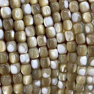 Peut inclure: Gros plan sur une collection de perles carrées. Les perles sont un mélange de blanc crème et de marron clair, avec une finition brillante. Les perles sont enfilées ensemble, créant une surface texturée. Les perles sont probablement destinées à la fabrication de bijoux.