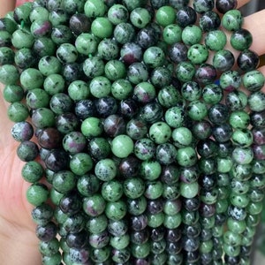 Könnte beinhalten: Eine Strähne grüner, schwarzer und rosafarbener Edelsteinperlen. Die Perlen sind rund und haben eine glatte, polierte Oberfläche.