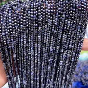 Può includere: Primo piano di una collana di perle di pietra preziosa blu scuro. Le perle sono rotonde e hanno una finitura liscia e lucida. La collana è composta da molte perle individuali, tutte di dimensioni approssimativamente uguali.
