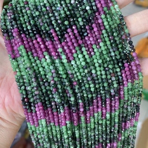 May include: A strand of green and pink gemstone beads. The beads are faceted and have a variety of shades of green and pink.