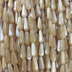 May include: A strand of iridescent, pearlescent, teardrop-shaped beads in a light beige color. The beads are strung on a clear thread and are arranged in a close-up view.
