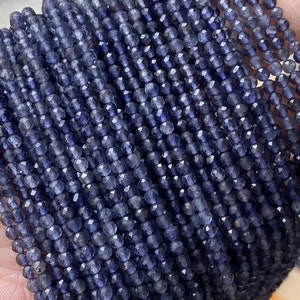 Puede incluir: Una hebra de cuentas de piedras preciosas facetadas de color azul oscuro. Las cuentas son pequeñas y redondas, y tienen un ligero brillo iridiscente.