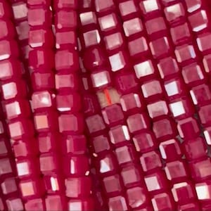 May include: Close-up of a strand of small, square, red glass beads. The beads have a slight iridescent sheen.