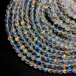Op de afbeelding: Close-up van meerdere strengen heldere, iriserende ronde kralen. Elke kraal reflecteert een regenboog van kleuren, waaronder blauw, geel en oranje. De kralen zijn aan elkaar geregen, waardoor een vloeiend patroon ontstaat. Geschikt voor het maken van sieraden.