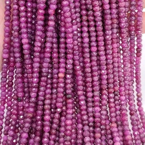Op de afbeelding: Een streng dieproze robijn kralen, elke kraal is gefacetteerd en heeft een ronde vorm. De kralen zijn geregen op een doorzichtige draad.