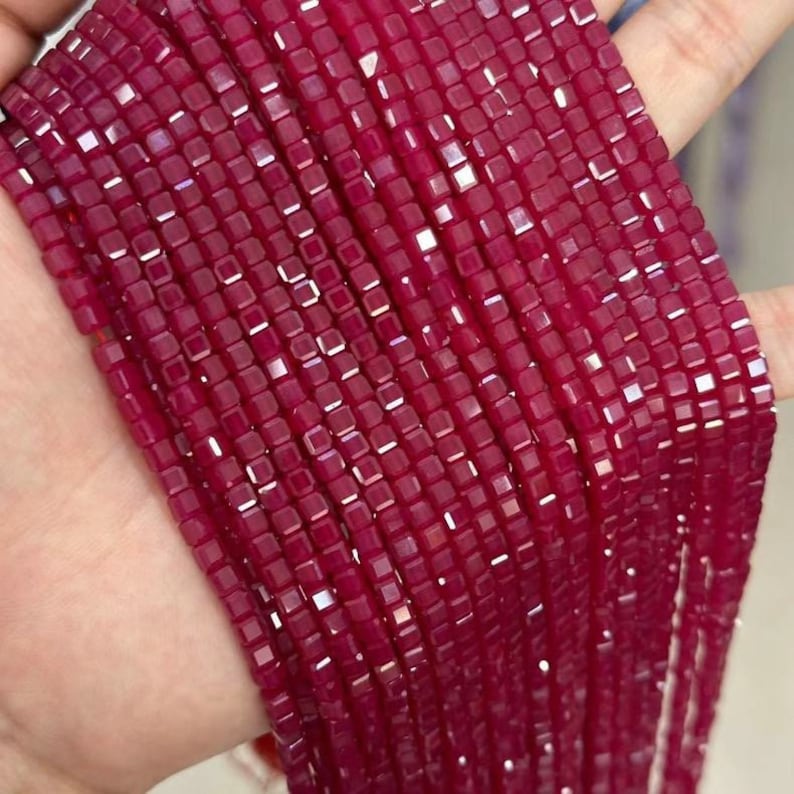 May include: A strand of ruby red square beads, each bead is faceted and has a shiny finish.