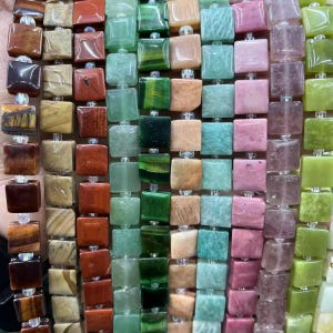 May include: Multiple strands of square-shaped gemstone beads arranged in vertical rows. The beads feature a variety of colors including brown, tan, red, green, light blue, pink, and purple, with some showing natural stone patterns and textures.