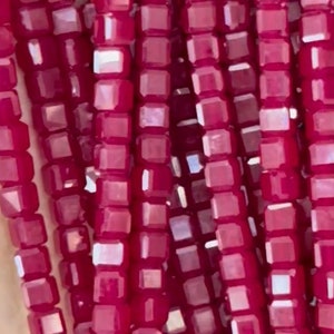 May include: A strand of small, square-shaped, faceted beads in a deep, rich burgundy color. The beads are strung together to create a continuous strand.