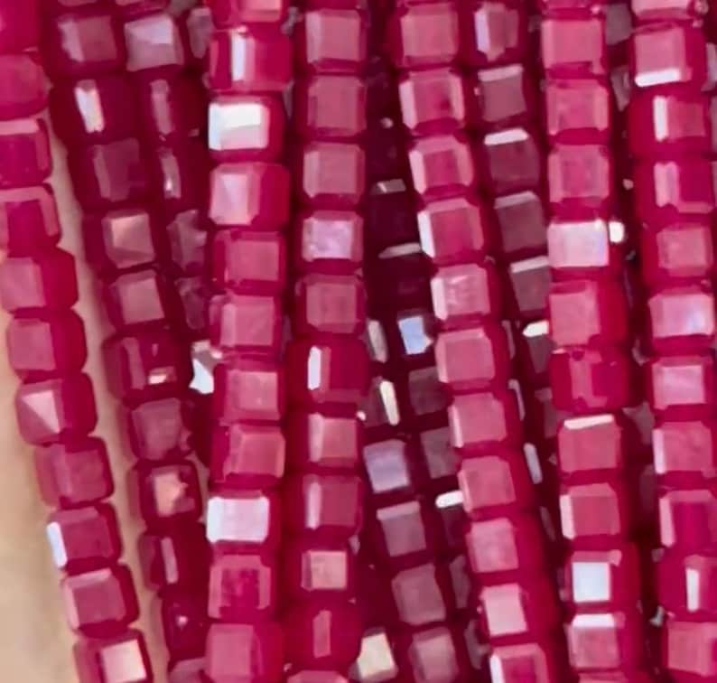 May include: A strand of small, square-shaped, faceted beads in a deep, rich burgundy color. The beads are strung together to create a continuous strand.