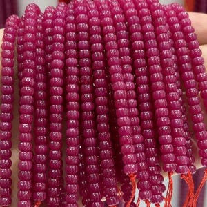 May include: Strands of deep magenta-colored beads. Each bead has a rounded, ridged shape, strung together with red thread. The beads are closely packed, creating a dense, textured appearance. Ideal for jewelry making.