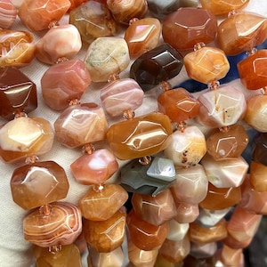 Könnte beinhalten: Eine Kette aus Karneol-Edelsteinen, jede Perle ist facettiert und hat ein einzigartiges orangefarbenes, braunes und weißes Muster. Die Perlen sind auf einer durchsichtigen Gummikordel aufgefädelt.