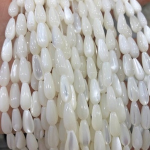 May include: A strand of white iridescent teardrop-shaped beads made from mother of pearl.