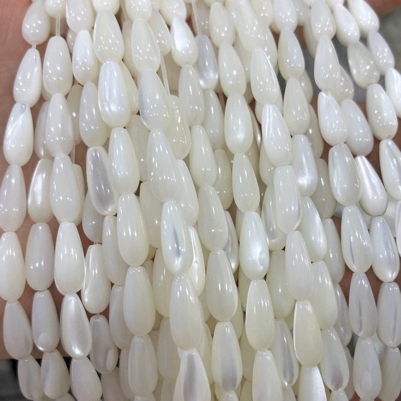 May include: A strand of white iridescent teardrop-shaped beads made from mother of pearl.