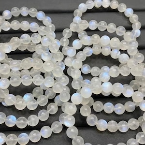 May include: A set of white moonstone bracelets with a iridescent sheen. The bracelets are made of round beads and are stacked on top of each other.