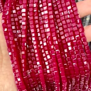 May include: A strand of small, square, red glass beads. The beads have a slightly iridescent finish.