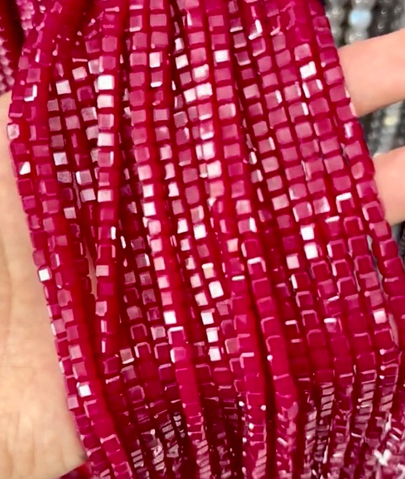 May include: A strand of small, square, red glass beads. The beads have a slightly iridescent finish.