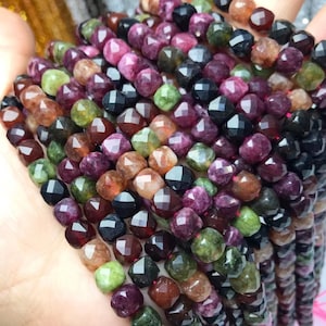 May include: A strand of faceted gemstone beads in various shades of green, red, brown, and black. The beads are all approximately the same size and shape, and they are strung on a clear thread.