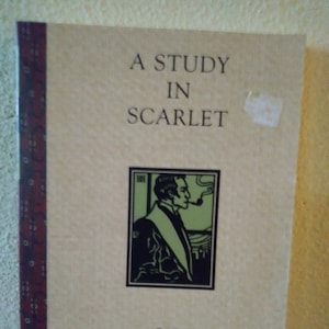 May include: A Study in Scarlet by Sir Arthur Conan Doyle book cover with a black and white illustration of a man with a pipe.