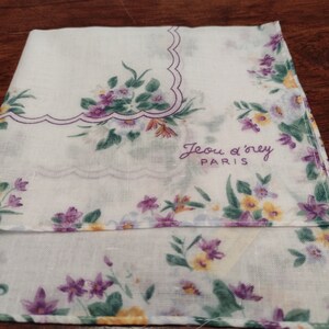 May include: White cotton handkerchief with a purple and yellow floral pattern. The handkerchief has a scalloped edge and the text "Jeu d'orey PARIS" embroidered in purple.