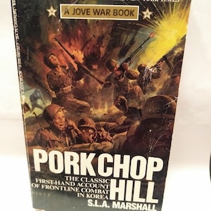 May include: A book cover featuring a dramatic illustration of soldiers in combat. The title is "Pork Chop Hill" and the author is S.L.A. Marshall. The book is described as "The Classic First-Hand Account of Frontline Combat in Korea".