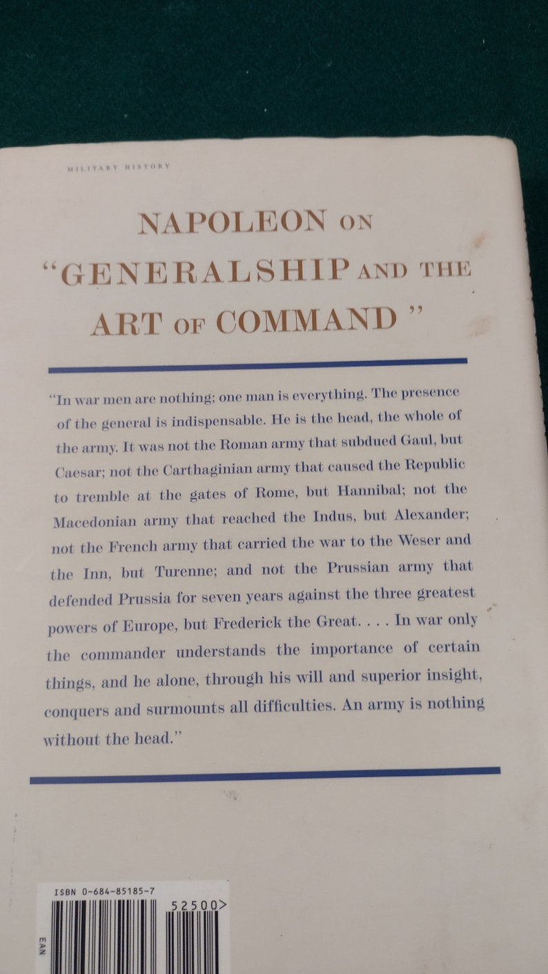 May include: A vintage book cover with a white background and brown text. The title is "Napoleon on "Generalship and the Art of Command". The text on the back cover is a quote from Napoleon about the importance of leadership in war.